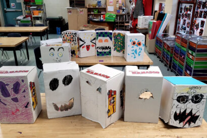 Puppets and Pageantry Grades 3-5 - Hanover Theatre and Conservatory Art classroom scene with decorated cardboard boxes arranged on wooden tables, each box featuring colorful drawings and faces.