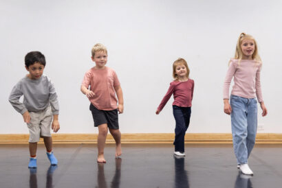 Storytime Drama Ages 4-5 - Hanover Theatre and Conservatory Four young children dancing in a studio with a gray wall and a wooden barre, wearing casual clothes.