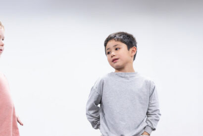 Storytime Drama Grades K-2 - Hanover Theatre and Conservatory Two young children stand apart against a pale background; a boy in a gray sweatshirt on the right looks toward the left, while a pink-shirted child is visible on the left.
