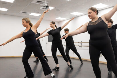 Teen Tap SUMMER - Hanover Theatre and Conservatory Group of dancers in black athletic wear performing a synchronized pose in a studio with a ballet barre along the wall