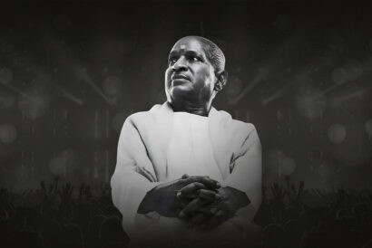 1920X1080-BOSTONjpg - Hanover Theatre and Conservatory Man in white traditional robes stands with folded hands on a dark stage, a cheering crowd silhouettes at the bottom.