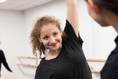 Acting 1: Monologues (Grades 8-10) - Hanover Theatre and Conservatory Smiling young woman with curly hair raises her arm in a dance studio, looking at a teacher.