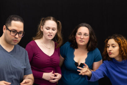 Adult Improv 1 Ages 18+ - Hanover Theatre and Conservatory Four adults sit closely together, looking down at something off-screen in a studio with a black backdrop.