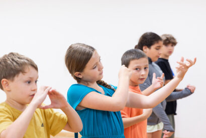 Beginner Improv 1 and Performance Grades 5-6 - Hanover Theatre and Conservatory Children in a line practicing synchronized arm movements in a studio or classroom setting.
