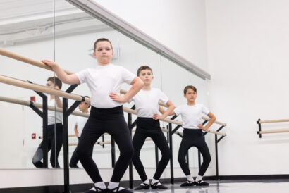 Boys Ballet Ages 8-18 - Hanover Theatre and Conservatory Three boys in white shirts and black pants pose at a ballet barre in a mirrored studio, hands on hips.