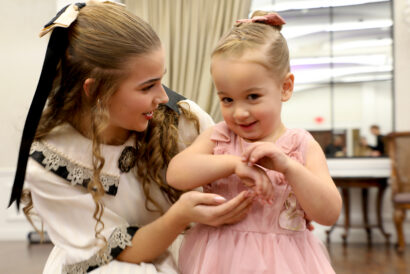 Clara_1920 x 1080 hero image - video card - FB event - Hanover Theatre and Conservatory Clara, a young girl dressed in a white dress with lace details and a bow in her hair, talking to a toddler in a pink dress during Cookies and Tea.