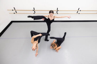 Contemporary Acro 2 - Hanover Theatre and Conservatory Four dancers practice in a ballet/studio space with a barre; one stands in arabesque while others stretch on the floor. 1/4 place in black outfits.