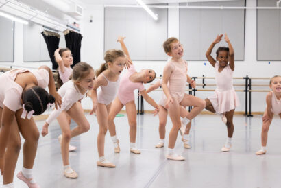Creative Movement Ages 5-6 - Hanover Theatre and Conservatory Group of young girls in pale pink leotards and tights doing ballet warm-ups in a studio with mirrors and a barre along the wall.
