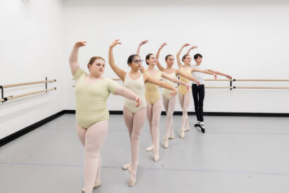Focus Group Invitation Only - Hanover Theatre and Conservatory Group of young ballet dancers in pastel leotards standing at a ballet barre, practicing arm positions in a studio.
