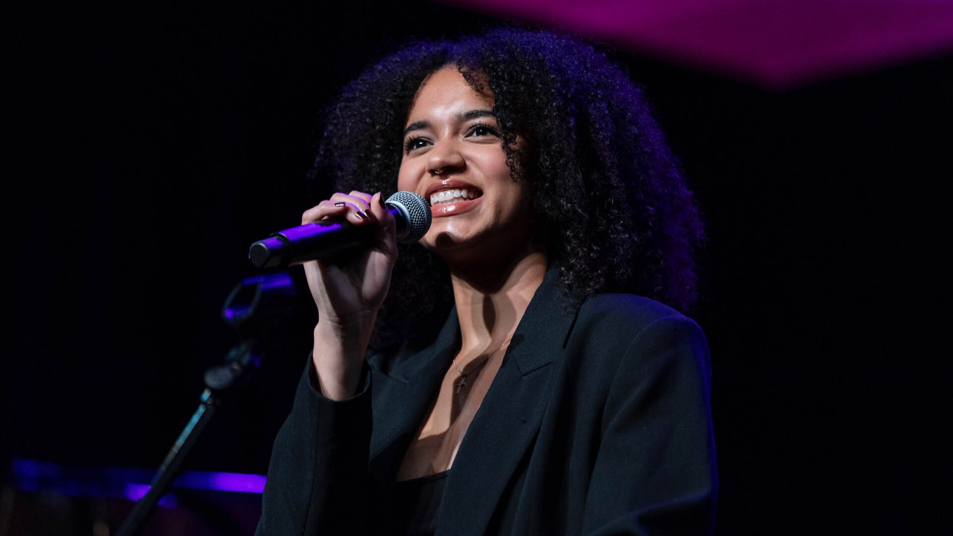Georgia Heers - Hanover Theatre and Conservatory Female singer on stage, mid-performance, holding a microphone and smiling under purple stage lighting.