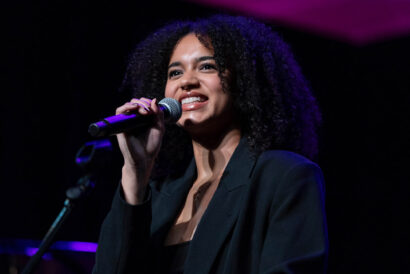 Georgia Heers - Hanover Theatre and Conservatory Female singer on stage, mid-performance, holding a microphone and smiling under purple stage lighting.