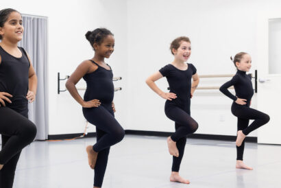 Jazz 1 Ages 8+ - Hanover Theatre and Conservatory Four young girls in black leotards practicing ballet in a dance studio with barres along the wall.