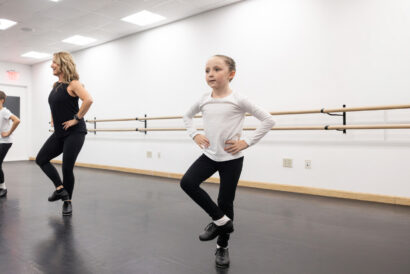 Primary Tap 1 Ages 7-9 - Hanover Theatre and Conservatory Instructor and two young dancers practice at a ballet barre in a bright dance studio.