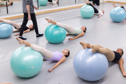 Progessing Ballet Technique Junior Level - Hanover Theatre and Conservatory Fitness class in a studio where students lie on their backs with legs raised on large exercise balls, instructor standing nearby.