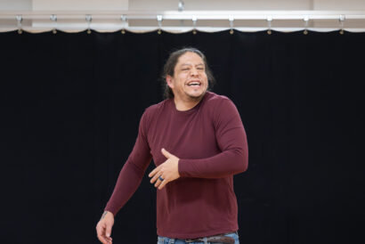 Stand-Up Comedy Ages 18+ - Hanover Theatre and Conservatory Smiling man with long hair in a maroon shirt performing on a stage with a black backdrop.