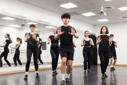 Teen Tap 1 Ages 12-18 - Hanover Theatre and Conservatory Group of dancers in a studio practicing a choreographed pose with hands held up, facing a wall of mirrors.