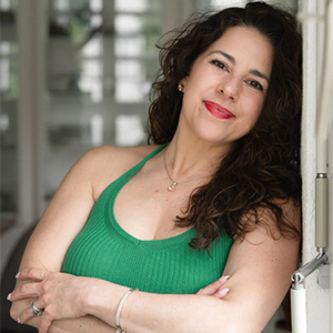 Jennifer Agbay - Hanover Theatre and Conservatory - Hanover Theatre and Conservatory Woman with long dark hair wearing a green sleeveless top, leaning against a doorway and smiling at the camera.