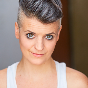 Molly Brennan headshot - Hanover Theatre and Conservatory - Hanover Theatre and Conservatory Close-up portrait of a woman with short gray hair and a white sleeveless top, looking at the camera with a gentle smile.